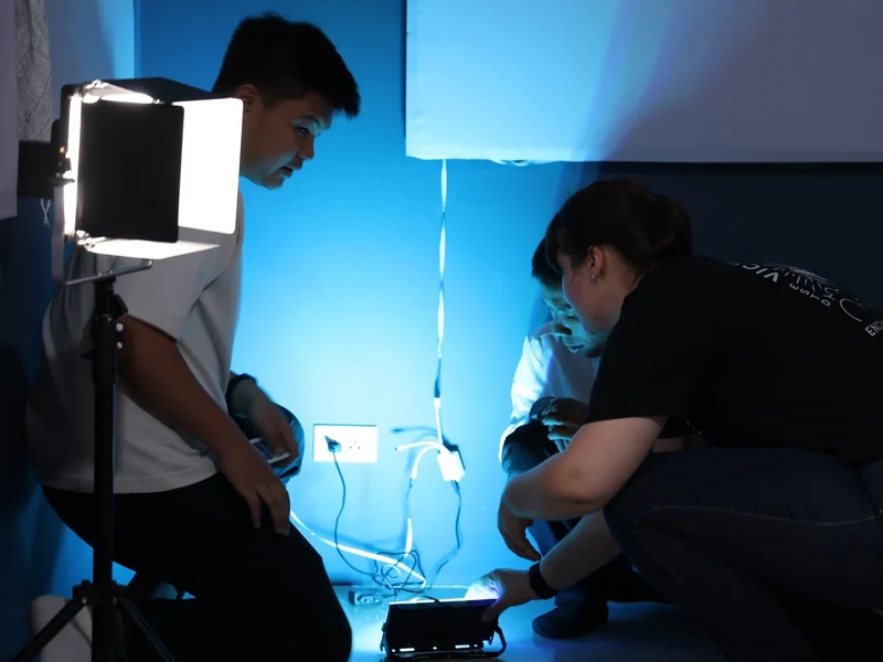 Two crew members crouched on the floor wiring an LED panel and softbox, the room lit blue by the panel's glow