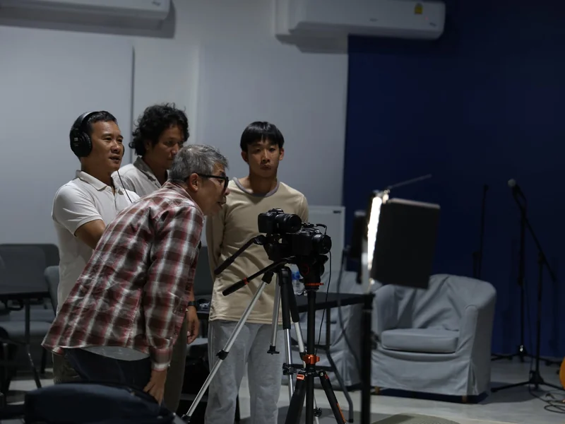 Four crew members huddled around a camera on a tripod, checking a shot together in the studio