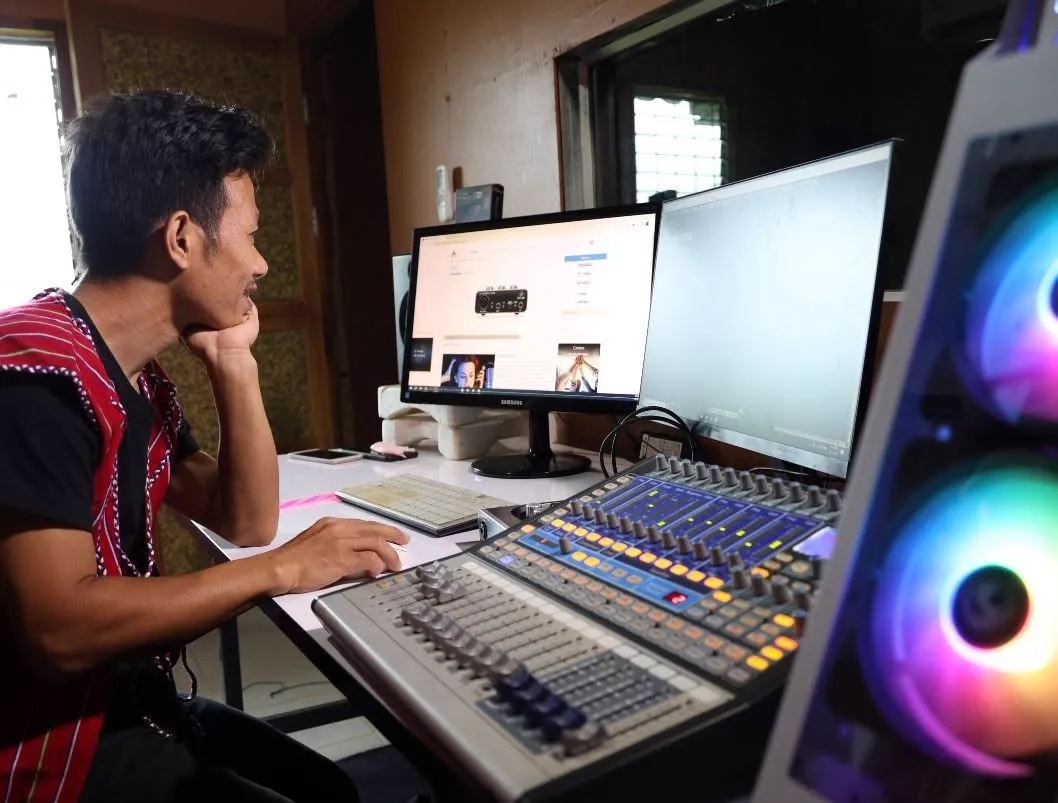 Project Video editor at a dual-monitor desk with an audio mixing board