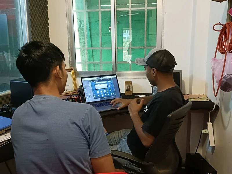Two sound editors leaning over a laptop, dialing in an audio plugin together at a small studio desk