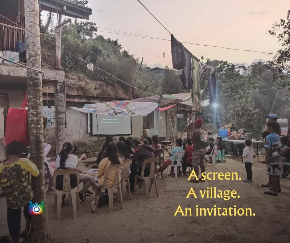 A screen. A village. An invitation. — a projector screen rigged between houses in a highland village at dusk