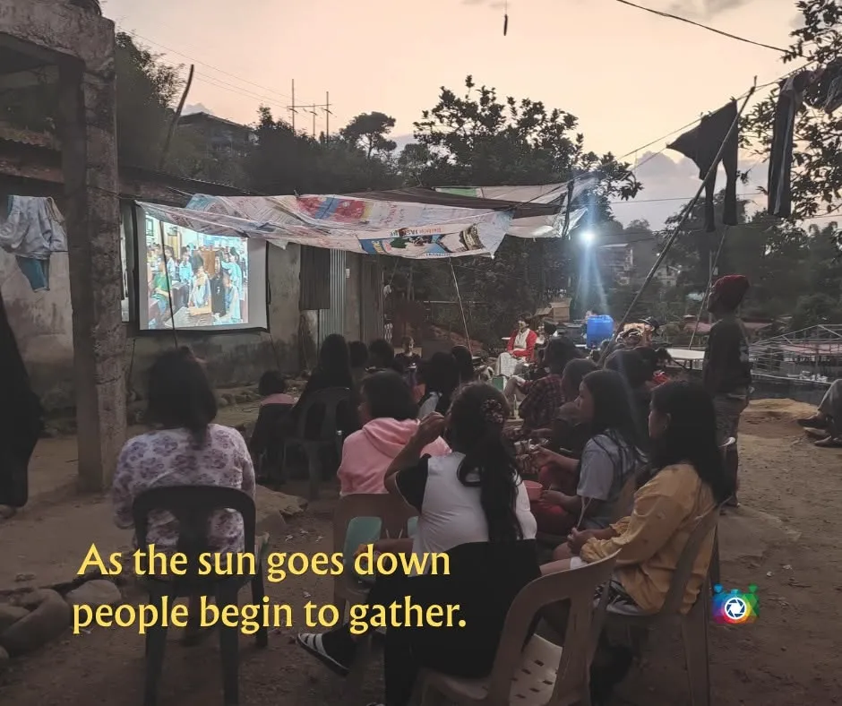 As the sun goes down, people begin to gather — villagers taking seats in front of the screen
