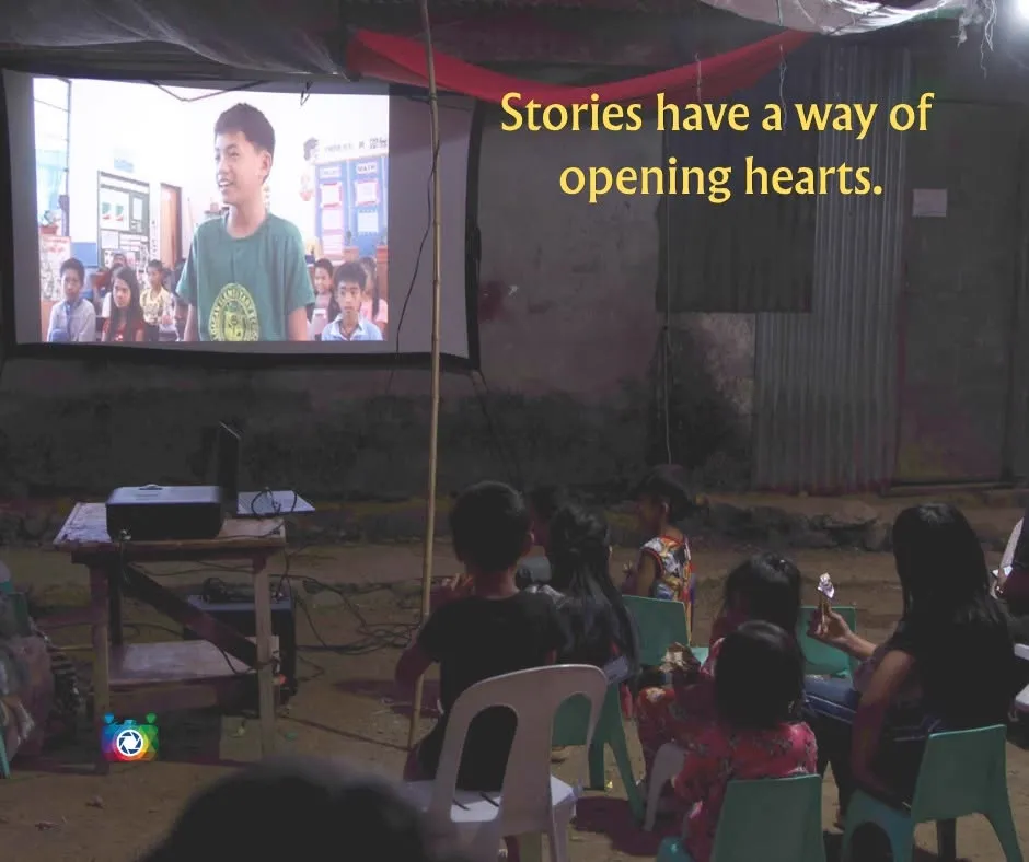 Stories have a way of opening hearts — children watching a film projected on an outdoor screen